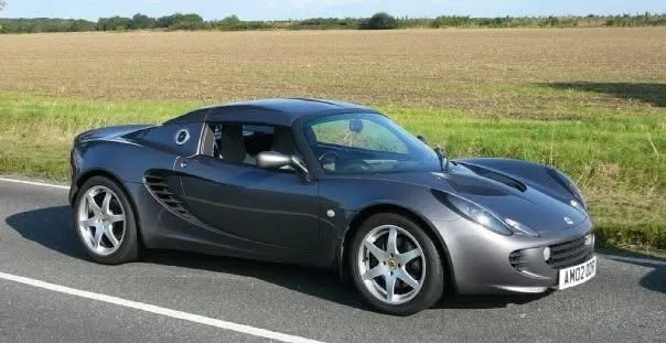 A grey Lotus Elise Sports Car, parked on the road with a field in the background.