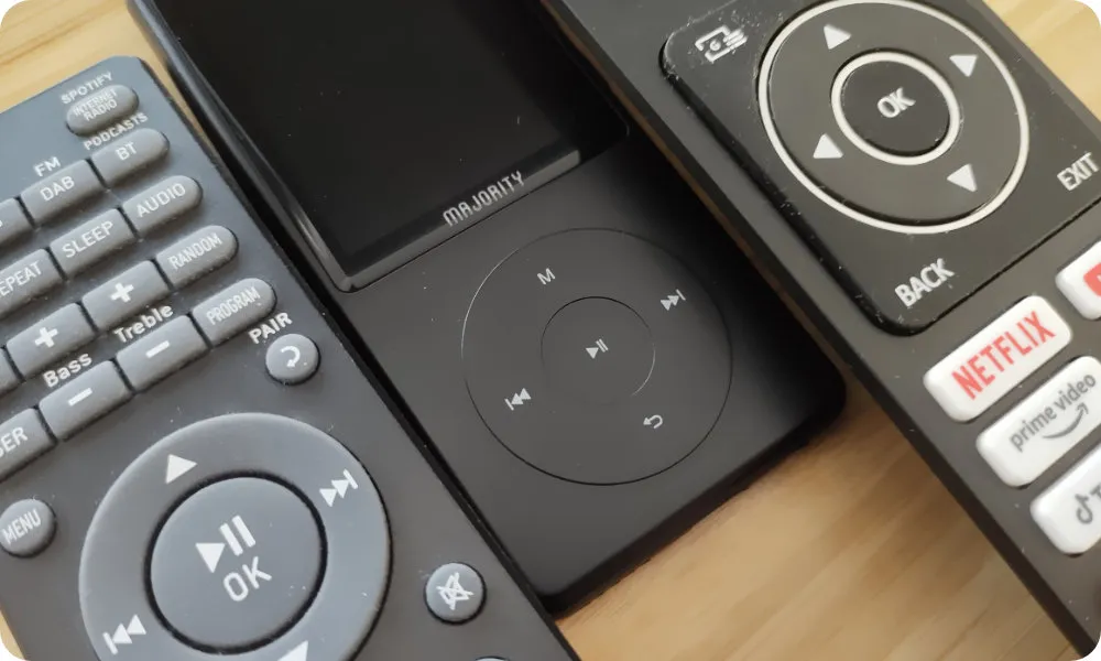 A HiFi remote, The Majority MP3 Pro and a TV remote are aligned side-by-side. The arrangement emphasis that all three devices have a compass-like navigational control button pattern.