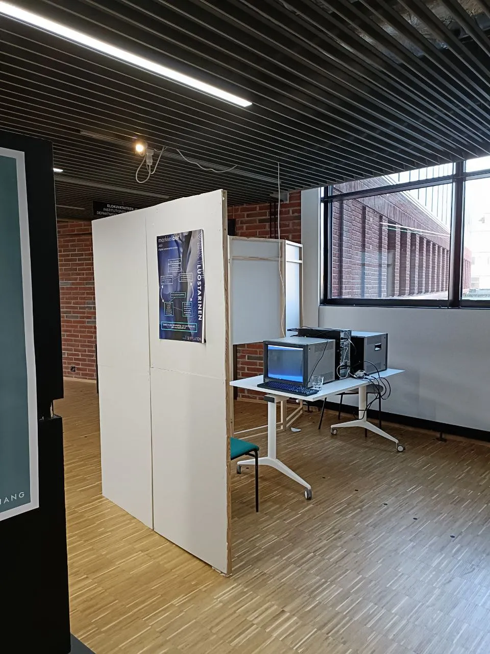 An installation that consists of two old televisions on a table, facing the opposite way. On two sides, the table is surrounded by a white folding screen.